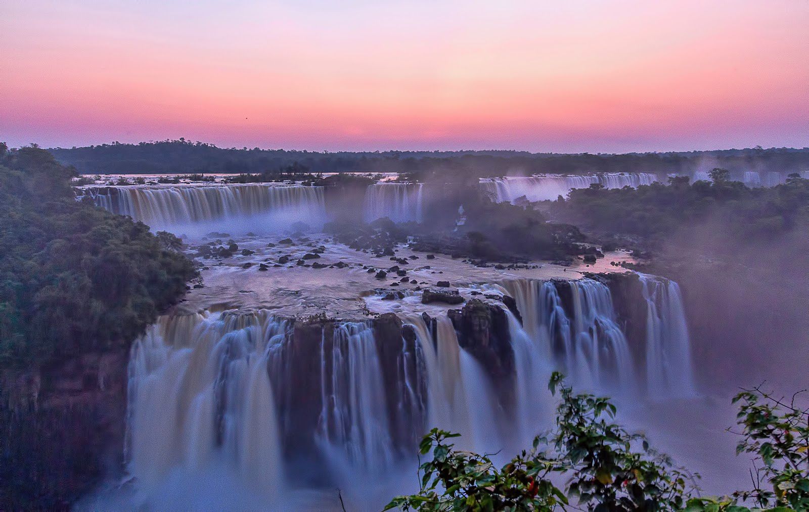 Iguazu Falls cascading into the Devil's Throat chasm, surrounded by lush rainforest.