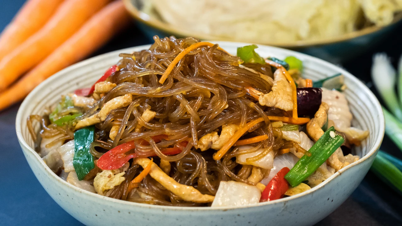 Sepiring bihun goreng dengan sayuran segar dan irisan telur, disajikan hangat dengan bumbu gurih yang khas