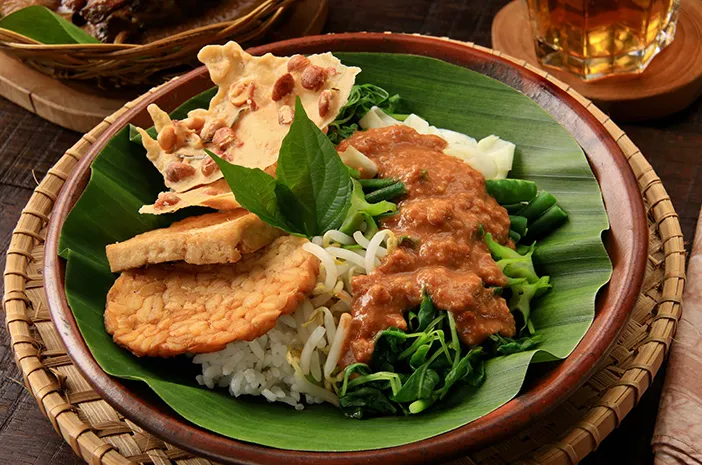 Tampilan dekat pecel sayur dengan bumbu kacang melimpah dan sayuran segar, disajikan dengan rempeyek