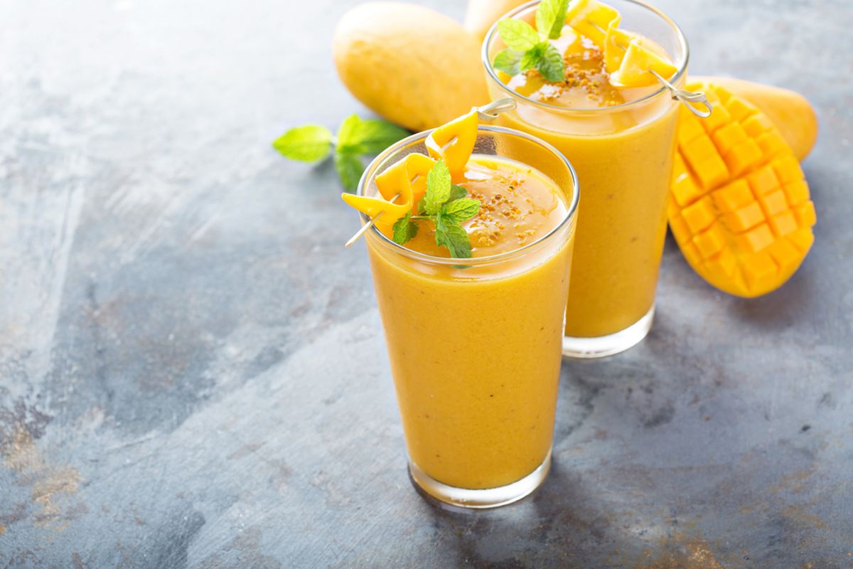 Segelas mocktail mangga tropis yang segar, dihiasi daun mint dan irisan lemon, siap dinikmati di hari yang cerah